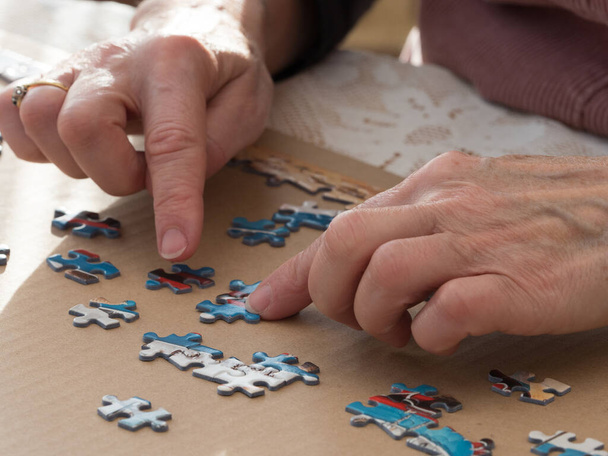 A close view of lady's hands moving jigsaw pieces with fingers on puzzle - Photo, Image