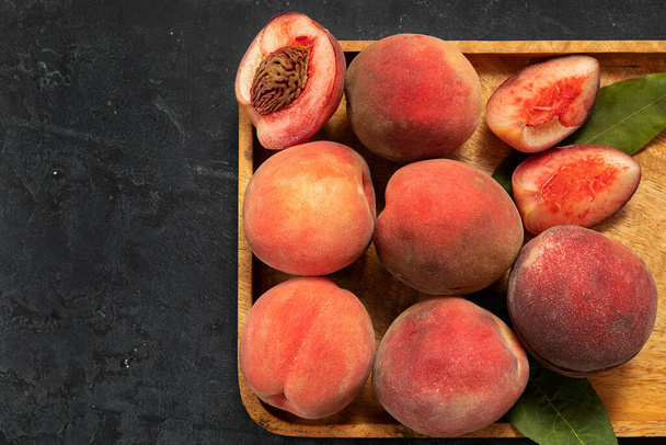 сочные спелые персиковые фрукты на деревянном блюде, на темном фоне. сельскохозяйственная продукция, концепция сезона сбора урожая. - Фото, изображение