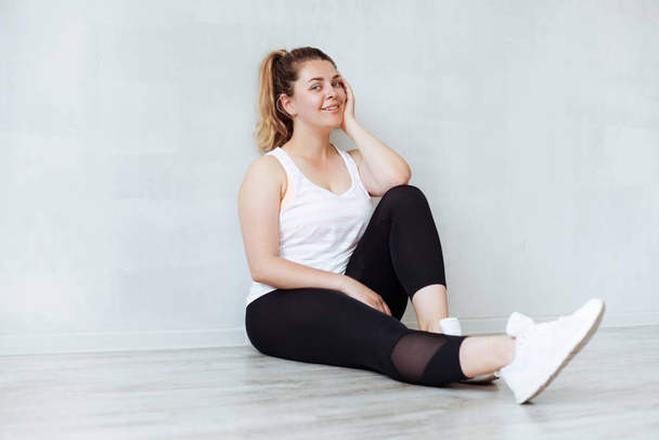 Beautiful sporty woman sitting on the floor and relaxing after training - Foto, afbeelding