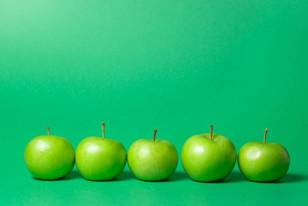 Grüne Äpfel auf grünem Hintergrund. Die Äpfel stehen in einer Reihe. Oben ist Platz für eine Inschrift oder ein Logo - Foto, Bild