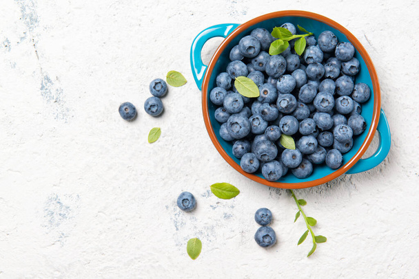 Fresh ripe blueberries with leaves in a bowl on a stone table, top view with copy space - Photo, image