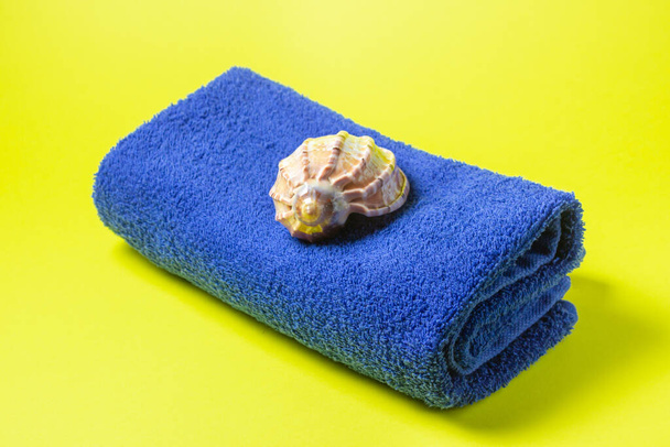 Toalla azul sobre fondo amarillo. La concha está sobre una toalla. Unas vacaciones tan esperadas. Un viaje al mar
. - Foto, Imagen