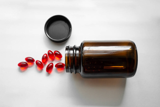 Een pot rode pillen. Tabletten gegoten uit de pot op witte achtergrond. Glazen bruine pil fles - Foto, afbeelding