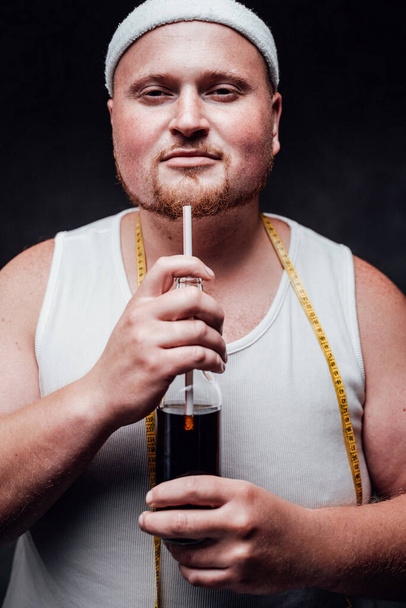 Hombre calvo grueso en ropa deportiva blanca, con una botella de cola en las manos
 - Foto, Imagen