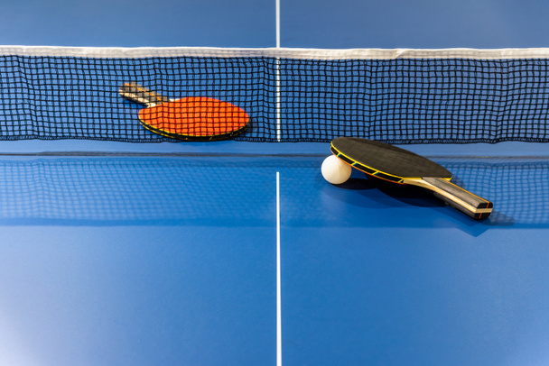 racchetta da ping pong nera e rossa e una palla bianca sul tavolo da ping pong blu con una rete, due paddle da ping pong è un'attrezzatura da competizione sportiva attività indoor ed esercizio per concetto di fondo - Foto, immagini