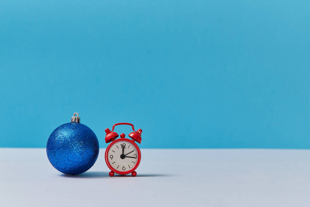 Bright shiny ball for decor. Red clock showing twelve oclock. Happy new year. Xmas concept. Copy space. Blue backdrop - Foto, Imagen