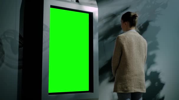 Mulher olhando para quiosque de exibição verde em branco na exposição conceito de tela verde - Filmagem, Vídeo