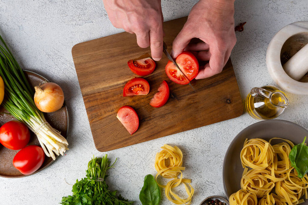Ruce sekání rajčata pro těstoviny vaření na bílém stole - Fotografie, Obrázek
