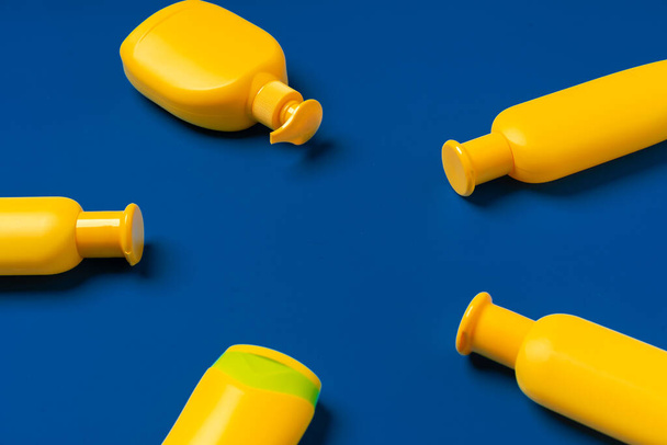 Bright yellow bottles of sunscreen product on dark blue paper background - Fotoğraf, Görsel