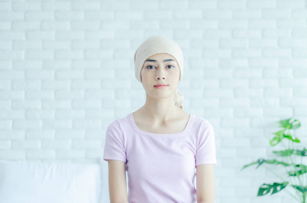 Las mujeres usan camisas rosas y vendajes para el cabello en una habitación blanco.La señora está enferma de cáncer.Una mujer asiática descansó en la habitación de la mañana.. - Foto, Imagen