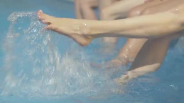 Slim female Caucasian feet splashing water in swimming pool at resort. Unrecognizable young women resting on sunny summer day outdoors. Tourism, leisure, relaxation, lifestyle. - Video, Çekim