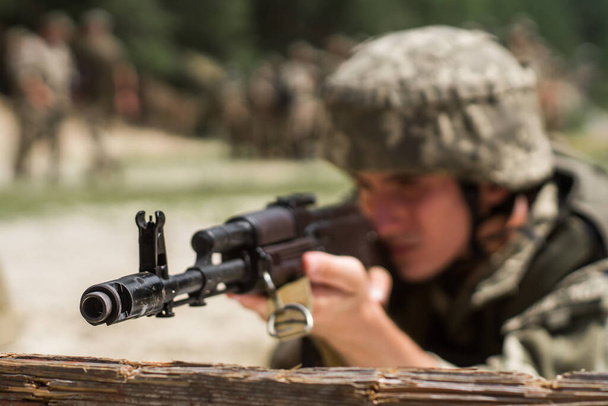 Close-up van een soldaat die mikt met een machinegeweer klaar om te vuren. Selectieve focus. De soldaat mikt met een AK 74. - Foto, afbeelding