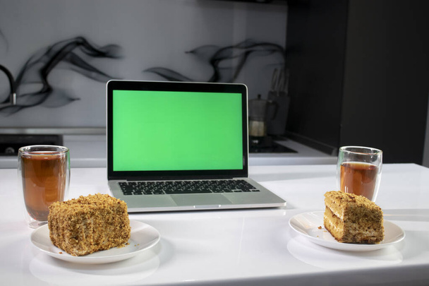 дві чашки чаю і два шматочки торта в сірій кухні поруч з ноутбуком з зеленим екраном хромати
 - Фото, зображення