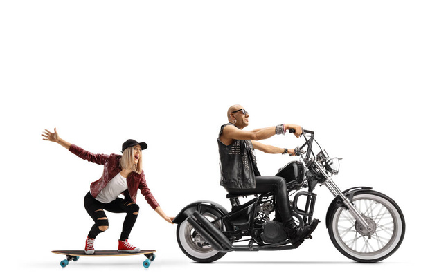 Man riding a chopper and a young female riding a skateboard and holding onto the motorbike isolated on white background - Foto, Bild