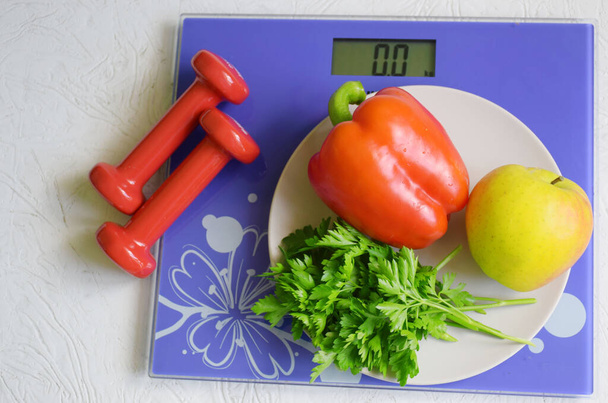 The concept of diet, vegetables and dumbbells and scales on a wooden background - Foto, Bild