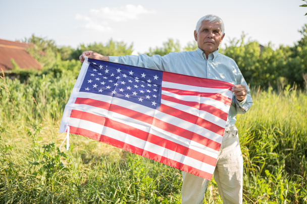 Patriotic senior man celebrates usa independence day on 4th of July with a national flag in his hands. Constitution and Citizenship Day. National Grandparents day - Photo, Image