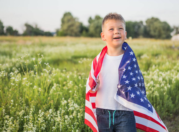 Fiatal fiú 4 éves kezében egy amerikai zászló naplementekor a mezőn. Alkotmány és hazafiság napja. - Fotó, kép