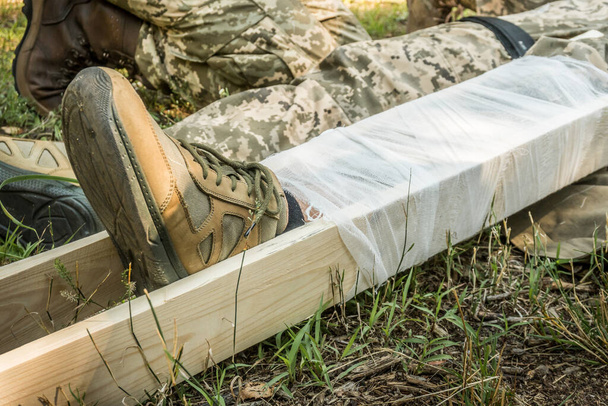 La pierna dañada del soldado se fijó con tablas y un vendaje. Medicina táctica. - Foto, Imagen