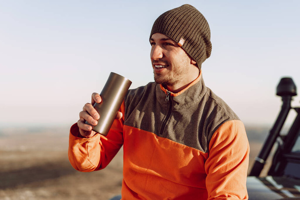 Young man traveler drinking from his thermocup while halt on a hike - Foto, imagen