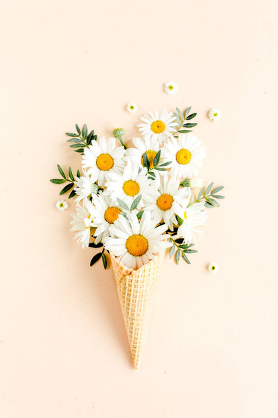 Waffle cone with chamomile flower, leaves on beige background. Flat lay, top view floral background. - Photo, image