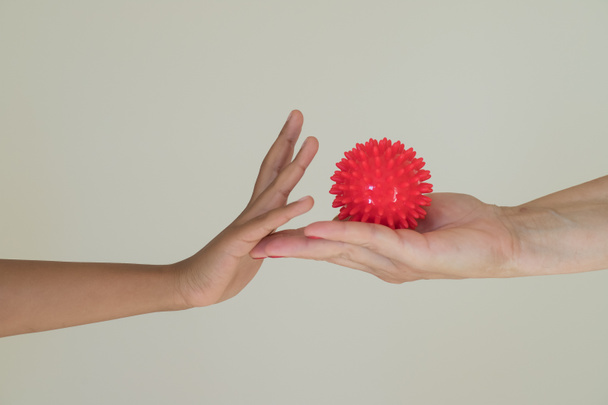 Red ball with spikes is a symbol of the Covid 19 virus in the hand of an adult, which passes it to the child.  Gesture of protection. Hygiene concept, the possibility of infection with the virus. - Photo, Image