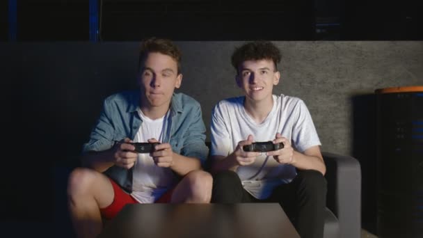 Veel plezier met de overwinning. Emotionele twee jonge jongens zitten op de bank voor de TV en opgewonden spelen een spelcomputer, met een joystick. Mens gaming met een draadloze controller. Donkere kamer - Video