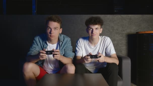 Twee overstuur jongens zitten op de bank voor de TV en verliezen in een spel op de console - Video