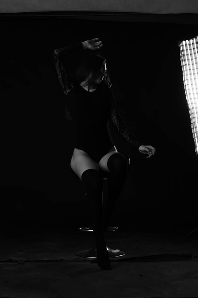 beautiful brunette young woman in black bodysuit posing on dark studio background  - Фото, изображение