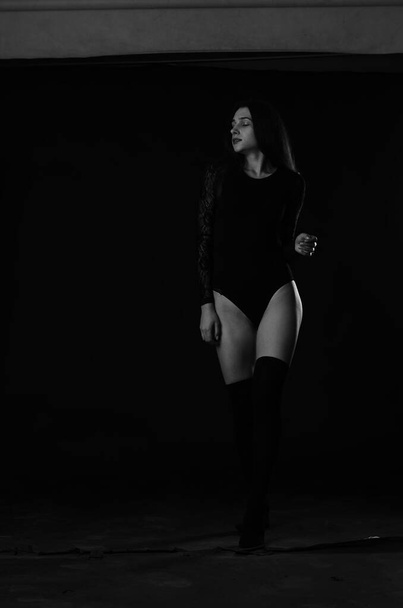 όμορφη μελαχρινή νεαρή γυναίκα με μαύρο κοστούμι που ποζάρει σε σκούρο φόντο στούντιο  - Φωτογραφία, εικόνα