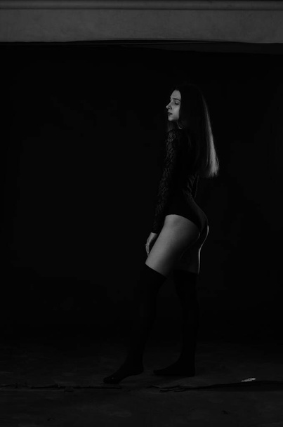 красивая брюнетка молодая женщина в черном боди позирует на темном фоне студии  - Фото, изображение