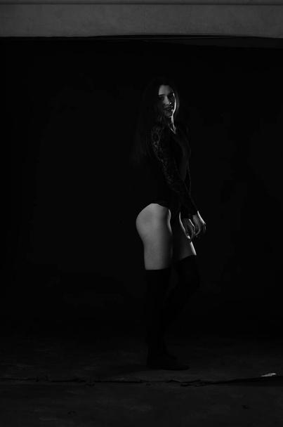 hermosa morena joven mujer en negro bodysuit posando sobre oscuro estudio fondo
  - Foto, Imagen