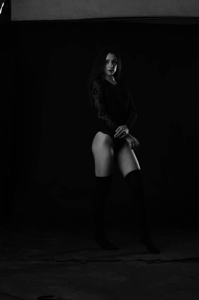 красивая брюнетка молодая женщина в черном боди позирует на темном фоне студии  - Фото, изображение