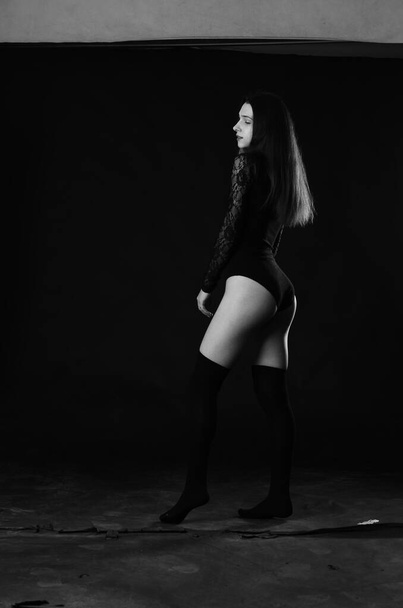 mooi brunette jong vrouw in zwart bodysuit poseren op donker studio achtergrond  - Foto, afbeelding