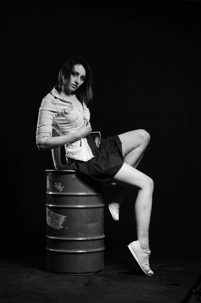 beautiful woman with short hear in stylish clothes posing with barrel on dark studio background   - Фото, изображение