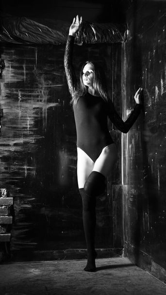 giovane donna in un body nero in posa su uno sfondo scuro, capelli neri e una figura sportiva muscolare. - Foto, immagini