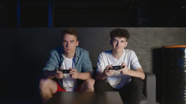 Δύο νεαροί φίλοι παίζουν βιντεοπαιχνίδι δράσης στο σαλόνι που κάθεται στον καναπέ. Ένας από αυτούς τελείωσε το παιχνίδι, είπε αντίο και έφυγε. - Πλάνα, βίντεο