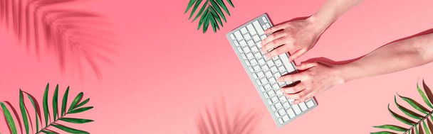 Person using a computer keyboard with tropical leaves - Фото, изображение