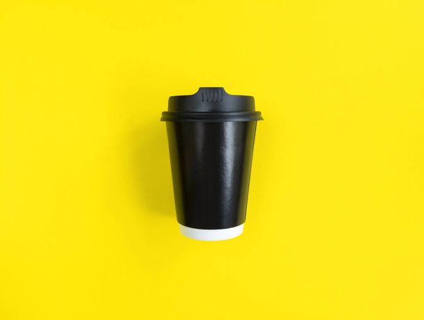 Μαύρο χάρτινο φλιτζάνι καφέ για να πάει στο κίτρινο backgroud. Επίπεδη στάση. Ελάχιστη έννοια. Στοκ φωτογραφία. - Φωτογραφία, εικόνα