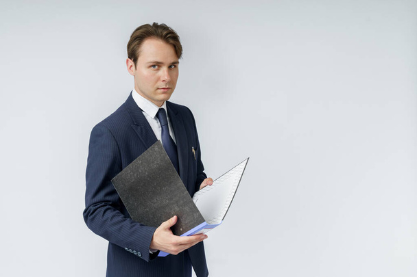 Un uomo d'affari in giacca e cravatta blu tiene cartelle su sfondo bianco. Concetto commerciale e finanziario - Foto, immagini