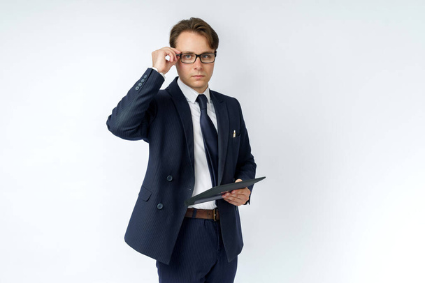 Retrato de un hombre de negocios con un traje azul que sostiene una tableta electrónica en sus manos y ajusta sus gafas. Fondo blanco. Concepto de negocio y finanzas - Foto, Imagen