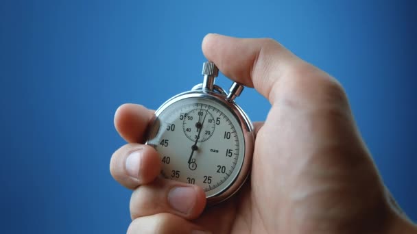 Male hand holding analogue stopwatch on blue color background. Time start with old chronometer man presses start button in the sport concept. Time management concept. - Footage, Video