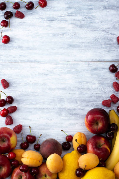 Pommes, bananes, pêches, abricots, pétioles, framboises sur fond gris clair. Fruits frais et lumineux. - Photo, image