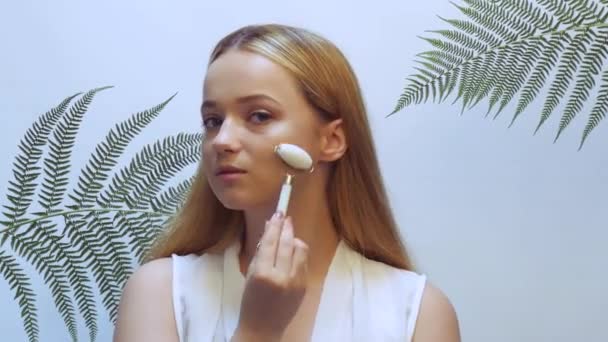 Belle fille dans les feuilles tropicales dans le studio touche son visage avec un rouleau - Séquence, vidéo