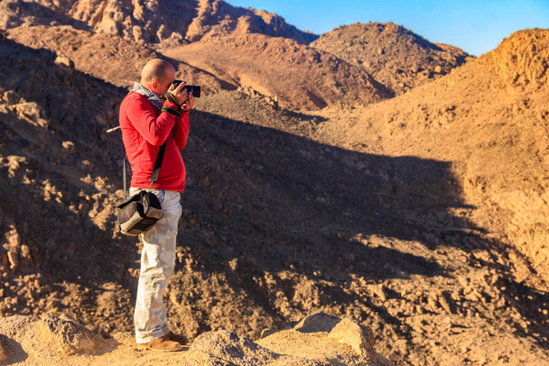 Młody człowiek robi zdjęcia pasma górskiego Red Sea Hills na pustyni arabskiej w Egipcie. Koncepcja fotografii podróżnej - Zdjęcie, obraz