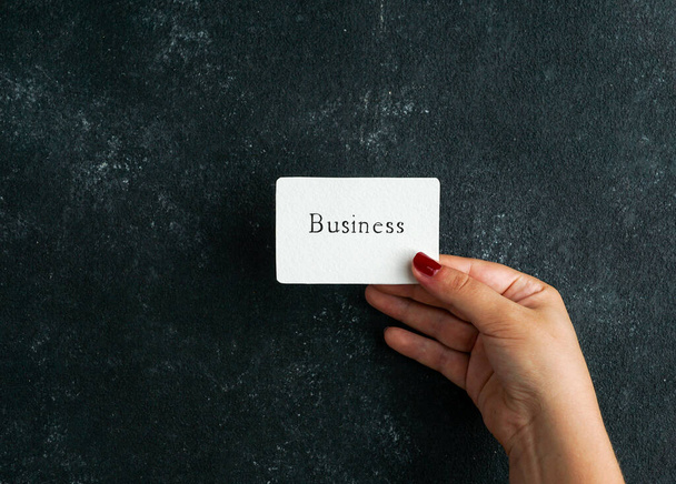consept d'affaires, carte de visite avec écriteau d'affaires dans la main des femmes tenant, sur le fond de béton noir - Photo, image