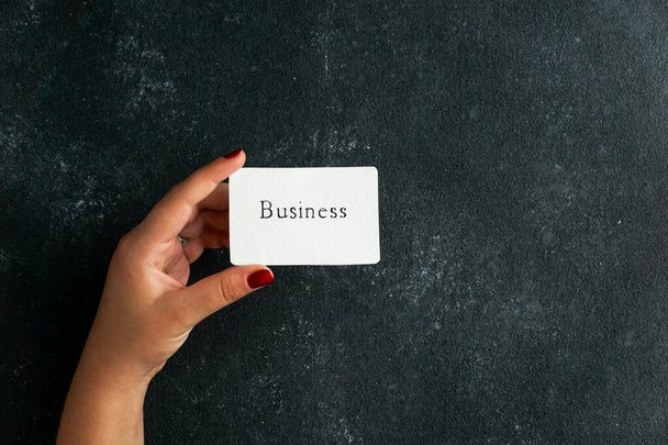 Business consept, visitekaartje met zakelijke geschriften in de hand van de vrouw, op de zwarte concret achtergrond - Foto, afbeelding