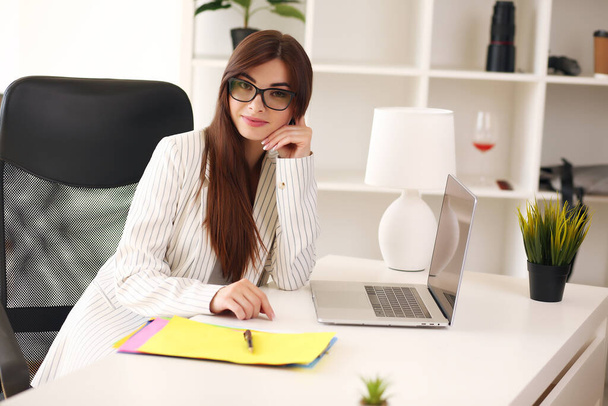 Beautiful business woman uses a laptop and smiles while working in the office - Foto, imagen