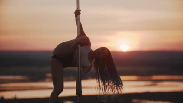Junge Frau mit langen Zöpfen tanzt und dreht sich bei Sonnenuntergang im Freien auf der Stange - Filmmaterial, Video