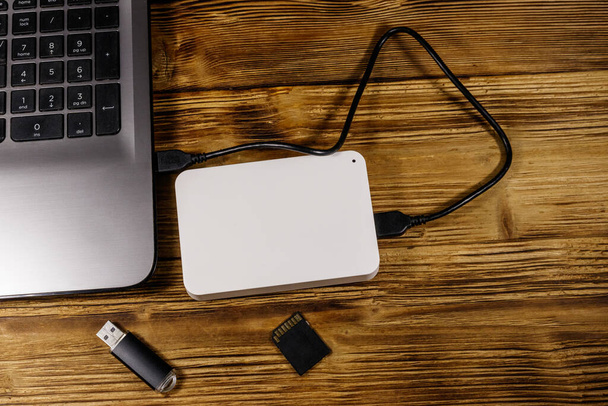 Externí HDD připojený k notebooku, SD paměťové kartě a USB flash disku na dřevěném stole. Horní pohled. Koncepce ukládání dat - Fotografie, Obrázek