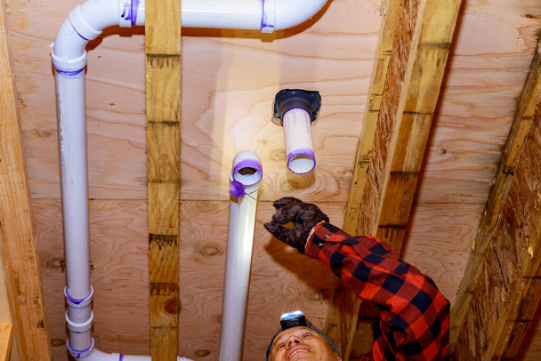 Υδραυλική κόλληση PVC πλαστικό αποχέτευσης τουαλέτα λευκό σωλήνα σε ξύλινο πλαίσιο οροφή δοκό του σπιτιού μαλακή εστίαση - Φωτογραφία, εικόνα